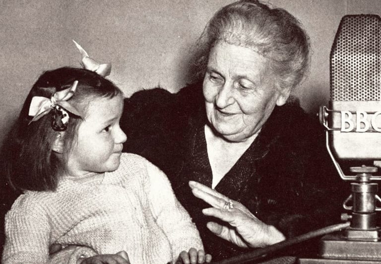 Maria Montessori seated beside a young child and a BBC microphone.