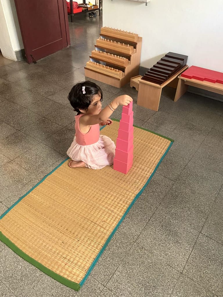 A young child places a pink cube on a tower on a floor mat.