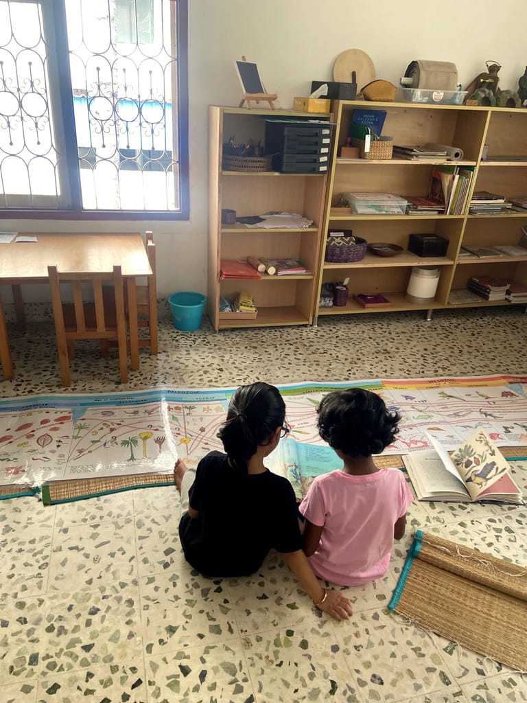 Two children sit side by side on a mat with an open book.